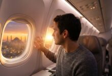 A man sits in a modern airplane seat, looking out the window at a breathtaking, softly focused view of the Istanbul, Turkey skyline during a beautiful sunrise, representing a journey for a hair transplant.