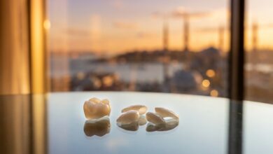 A close-up, photorealistic image of a perfect dental implant crown and veneers resting on a table, with the scenic, blurred skyline of Istanbul, Turkey visible in the background at sunset.