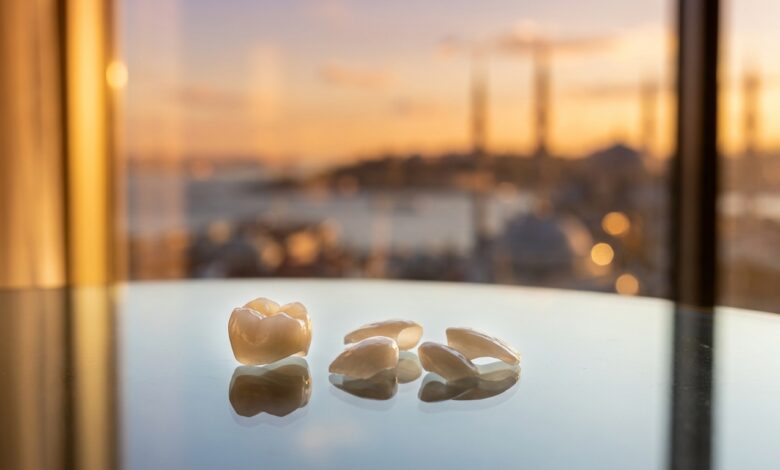 A close-up, photorealistic image of a perfect dental implant crown and veneers resting on a table, with the scenic, blurred skyline of Istanbul, Turkey visible in the background at sunset.
