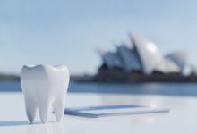 A close-up, photorealistic image of a sparkling white tooth on a clean surface, with blurred generic documents behind it. In the distant, highly blurred background, the distinct white sails of the Sydney Opera House are visible under a bright sky. The image conveys themes of dental health, policy, and financial considerations in Australia.
