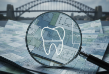 A close-up, photorealistic view of a magnifying glass held over a stack of abstract, layered financial documents or policy papers, which subtly incorporate conceptual dental motifs. The background is a blurred but recognizable Australian cityscape, emphasizing the local context. No text is visible.