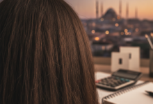 A photorealistic image focusing on the back of a head with healthy, dark hair in the foreground. Blurred in the mid-ground are abstract shapes suggesting financial planning tools like a calculator and notepad. In the heavily blurred background, a warm-lit Istanbul cityscape with domes and minarets is visible, representing medical tourism.