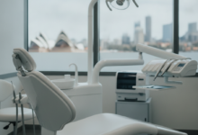 A clean, bright dental examination room in Sydney. An empty, ergonomic dental chair is in the foreground. Modern, sterile dental tools and equipment are blurred in the background. Through a window, a soft, out-of-focus view of the Sydney skyline is visible. The scene conveys professionalism and advanced dental care.