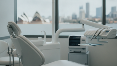 A clean, bright dental examination room in Sydney. An empty, ergonomic dental chair is in the foreground. Modern, sterile dental tools and equipment are blurred in the background. Through a window, a soft, out-of-focus view of the Sydney skyline is visible. The scene conveys professionalism and advanced dental care.